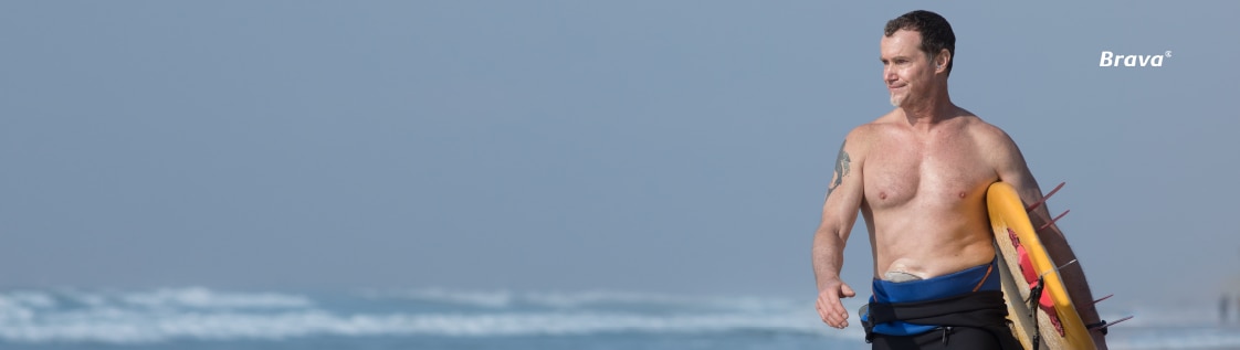 A smiling man walking on a beach with surf board.